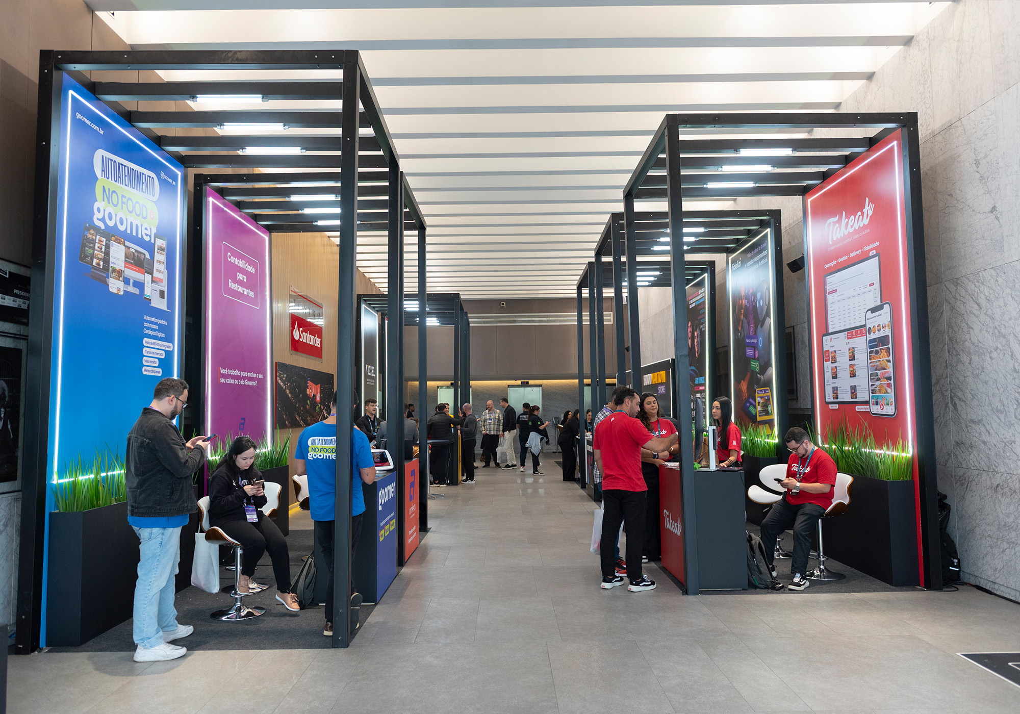 As pessoas interagem em vários estandes em um moderno espaço de exposição interno, com banners coloridos do Food Nation e displays informativos atrás de cada estande.