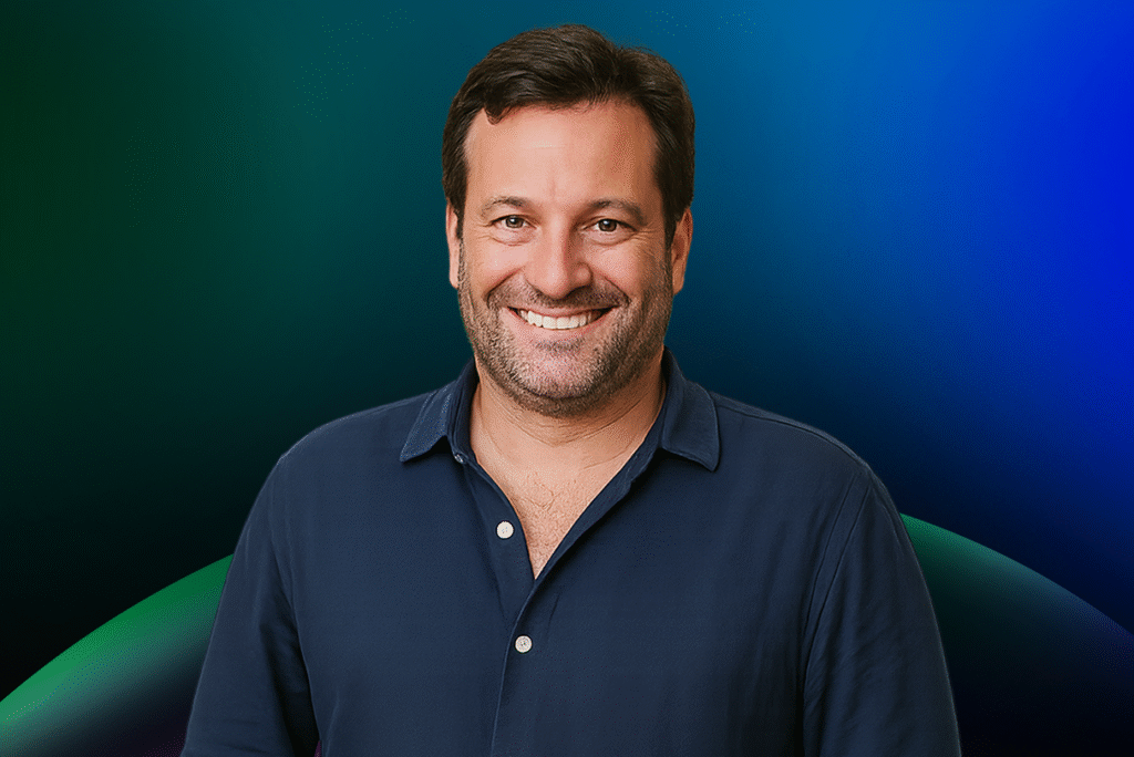 Homem sorridente, com cabelo escuro curto e barba, vestindo uma camisa azul escura, em frente a um fundo gradiente azul e verde, representando a Lista de Espera do Acelera Food Nation para 2026.