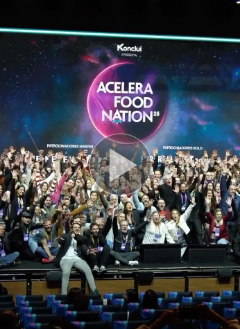 Um grande grupo de pessoas posa e torce no palco em frente a uma tela que exibe "Acelera Food Nation 25" em um evento interno, comemorando suas conquistas e olhando para o futuro do Acelera Food Nation 2026. Participe da Lista de Espera para receber atualizações!.