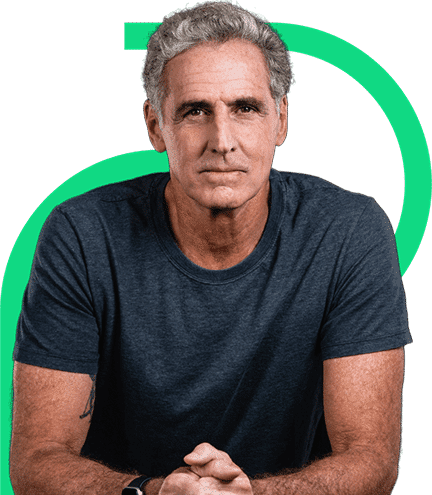 Um homem de meia-idade, com cabelos grisalhos curtos e camiseta azul-marinho, senta-se com as mãos cruzadas em frente a um fundo liso com uma linha curva verde.