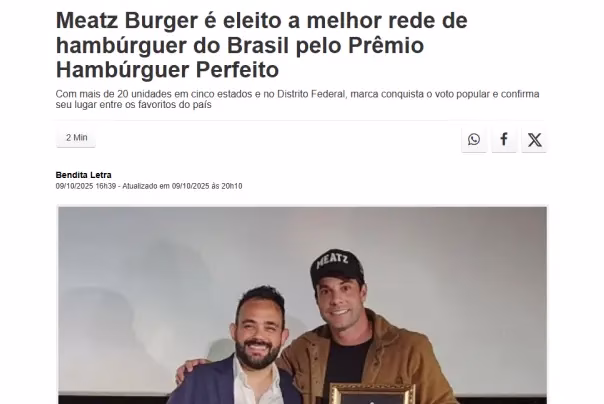 Dois homens posam juntos; um deles segura um prêmio emoldurado. A manchete acima diz: "Meatz Burger é eleito a melhor rede de hambúrgueres do Brasil pelo Prêmio Hambúrguer Perfeito.